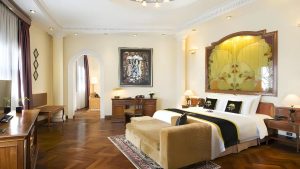 Phòng suite Indochine sử dụng sàn gỗ xương cá, nội thất gỗ và nghệ thuật làm trung tâm thị giác.