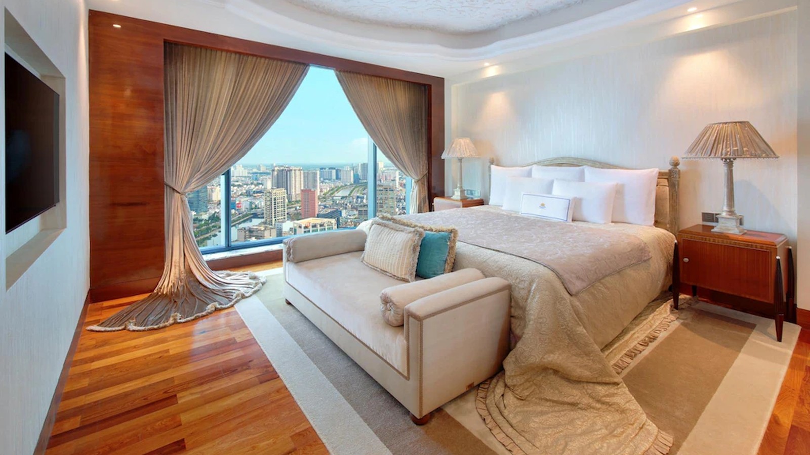 Phòng suite nổi bật với rèm dài, trần hoa văn và sofa cuối giường.