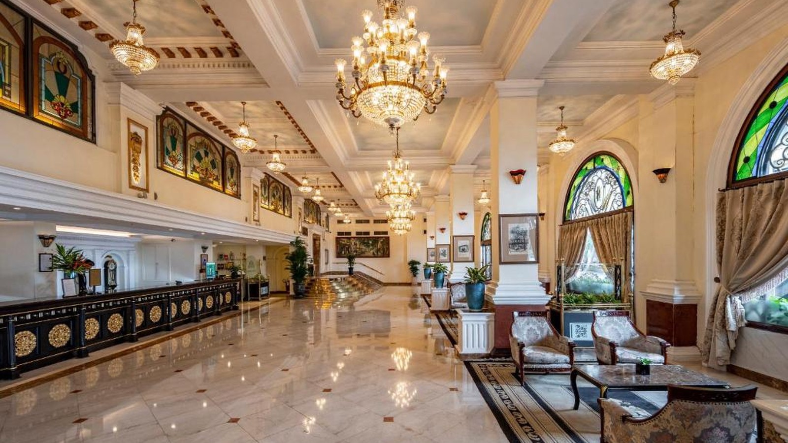 Lobby Indochine tạo chiều sâu bằng sàn đá sáng, cửa kính màu, rèm dày và các cụm ghế tiếp khách.