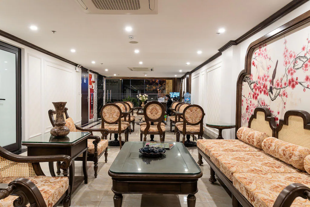 Phòng khách khách sạn 4 sao Indochine với sofa gỗ, ghế mây và tranh hoa đào