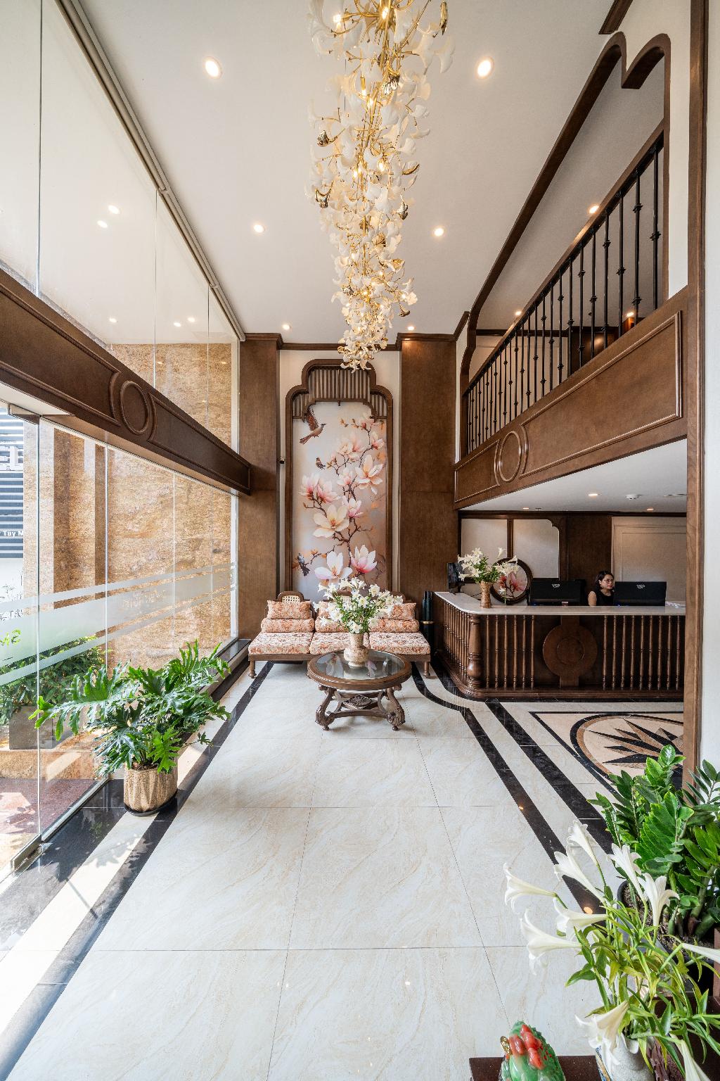 Sảnh lounge khách sạn 4 sao Indochine với ghế mây, gỗ sẫm và tranh hoa đào